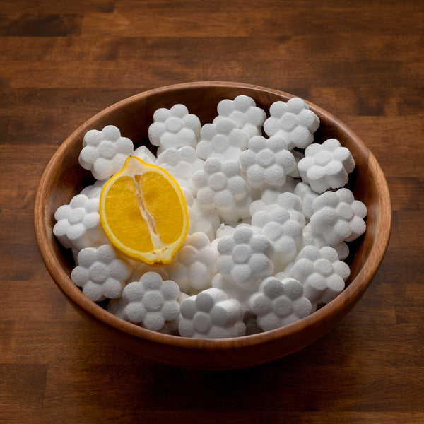 Lemon toilet cleaning pods in a wooden bowl with a lemon half